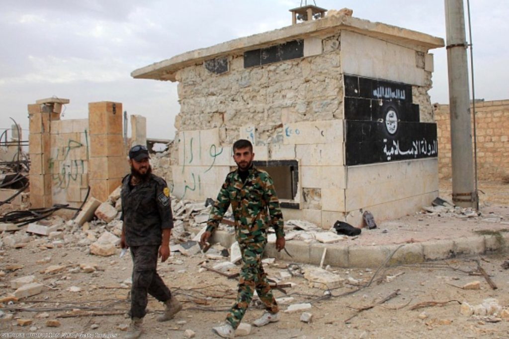 Syrian government forces walk past a building bearing an image on the wall with Islamic writing and reading in Arabic the 'Islamic State'